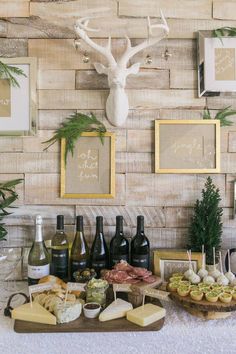 a table topped with wine bottles and cheeses next to framed pictures on the wall