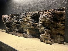 an aquarium with rocks and sand on the bottom floor, in front of a black wall