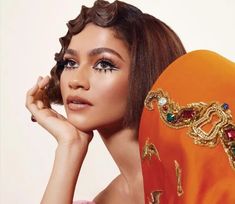 a woman in an orange dress with gold jewelry on her head and hands near her face