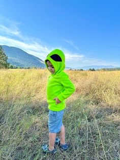 a little boy in a green hoodie standing in a field