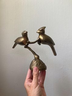 a hand holding a brass bird figurine with two birds on it's back