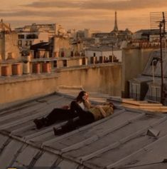 two people laying on top of a roof next to each other with buildings in the background