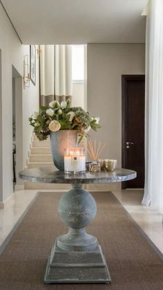 a vase with flowers and candles on a table in a room that has stairs leading up to the second floor