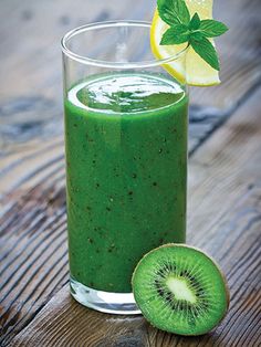 a green smoothie in a glass next to a sliced kiwi