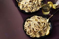 two black plates filled with pasta and lemon wedges