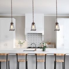 a kitchen with three pendant lights hanging from the ceiling and four bar stools at the counter