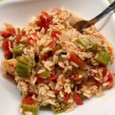 a white plate topped with rice and veggies next to a fork on a table