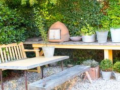 several potted plants sit on wooden benches in the middle of a graveled area