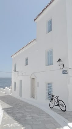 a bike parked in front of a white building next to the ocean on a sunny day