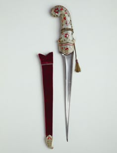 an elaborately decorated dagger with a red velvet case next to it on a white surface