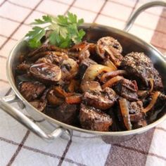 a pan filled with meat and vegetables on top of a table next to a napkin