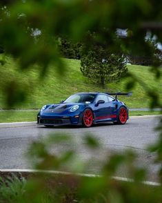 a blue sports car with red rims driving down the road in front of trees