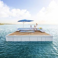 two people sitting on a floating platform in the water with an umbrella over them,