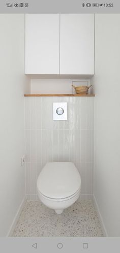 a white toilet sitting inside of a bathroom next to cupboards and a basket on the wall