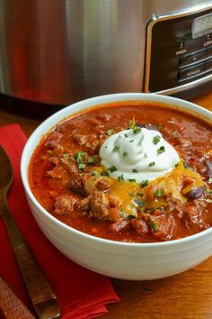 a bowl of chili with sour cream in it on a table next to a crock pot