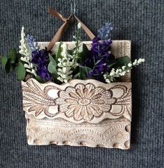 purple flowers are placed in an old wooden purse on the carpeted floor, hanging from a hook