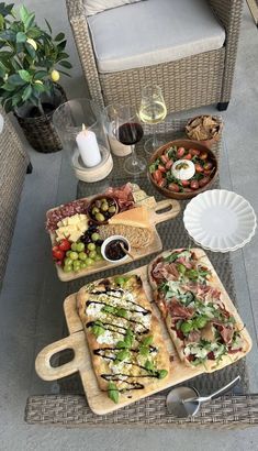 an outdoor table with pizzas and salads on trays next to wine glasses