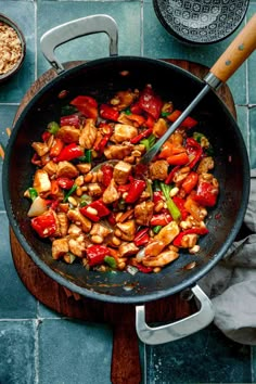 a wok filled with chicken and vegetables on top of a blue tiled countertop