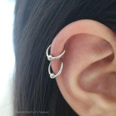 a woman's ear is shown with two small silver hoops