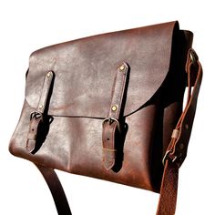 a brown leather messenger bag sitting on top of a white surface with straps around it