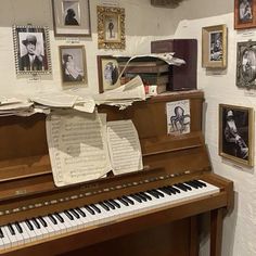 an old piano with sheet music on it in front of many framed pictures and photos