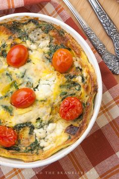 an omelet with tomatoes and spinach in a white bowl on a checkered table cloth