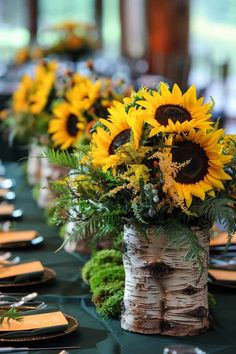 sunflowers and ferns are arranged in vases on a table with place settings