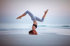 a woman doing a handstand on the beach with her feet in the air