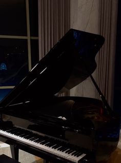 a black piano sitting in front of a window next to a wall with lights on it