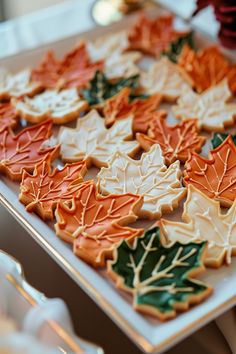 many decorated cookies are on a tray with silverware in the foreground and red, white, and green leaves