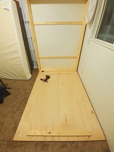 an open wooden bed frame sitting on top of carpeted floor next to a refrigerator