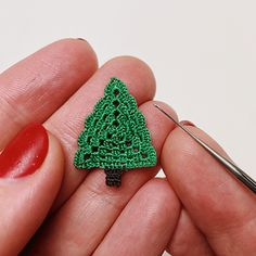 a crocheted green christmas tree brooch sits in someone's left hand