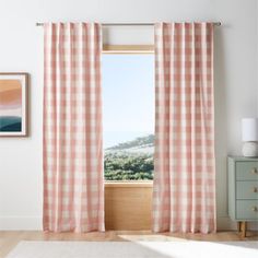 a window with pink and white checkered curtains hanging on the side of it, next to a dresser