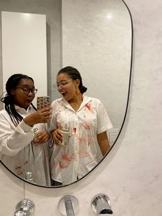 two women standing in front of a mirror with blood all over the walls and floor