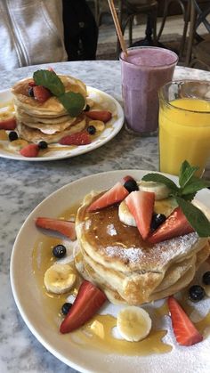 two plates with pancakes and fruit on them sitting on a table next to a glass of orange juice