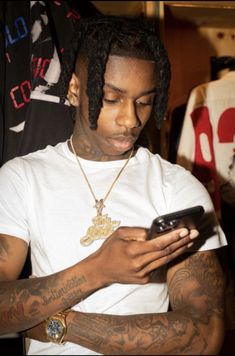 a man with dreadlocks looking at his cell phone while wearing a white t - shirt