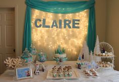 a table topped with cakes and desserts covered in frosted icing next to a blue curtain