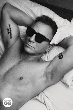 a shirtless man laying in bed with sunglasses on his head and tattoos on his arm