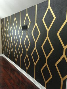 an empty room with black walls and gold geometric designs on the wall, along with wood flooring