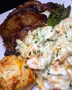 a white plate topped with meat and vegetables next to a biscuit covered in cheese