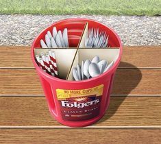 a red bucket filled with silverware sitting on top of a wooden table next to grass