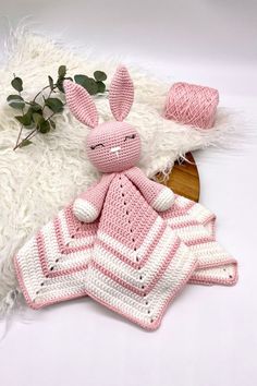 a crocheted bunny laying on top of a white rug next to a plant