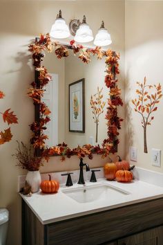 a bathroom decorated for fall with pumpkins and leaves on the mirror, along with two lights