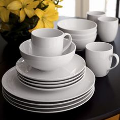 a black table topped with white plates and cups filled with yellow daffodils