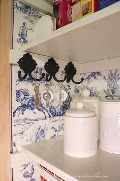 a kitchen shelf with two white canisters and some wallpaper on the walls