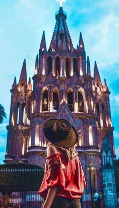 a woman wearing a hat standing in front of a tall building with a clock on it's side