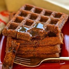 a red plate topped with waffles covered in syrup