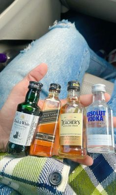 a person holding four bottles of alcohol in their hand and sitting on the back of a car