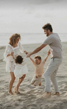 a family playing in the sand at the beach with their toddler's hands