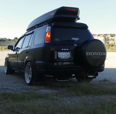 the back end of a black van parked on top of a parking lot next to grass